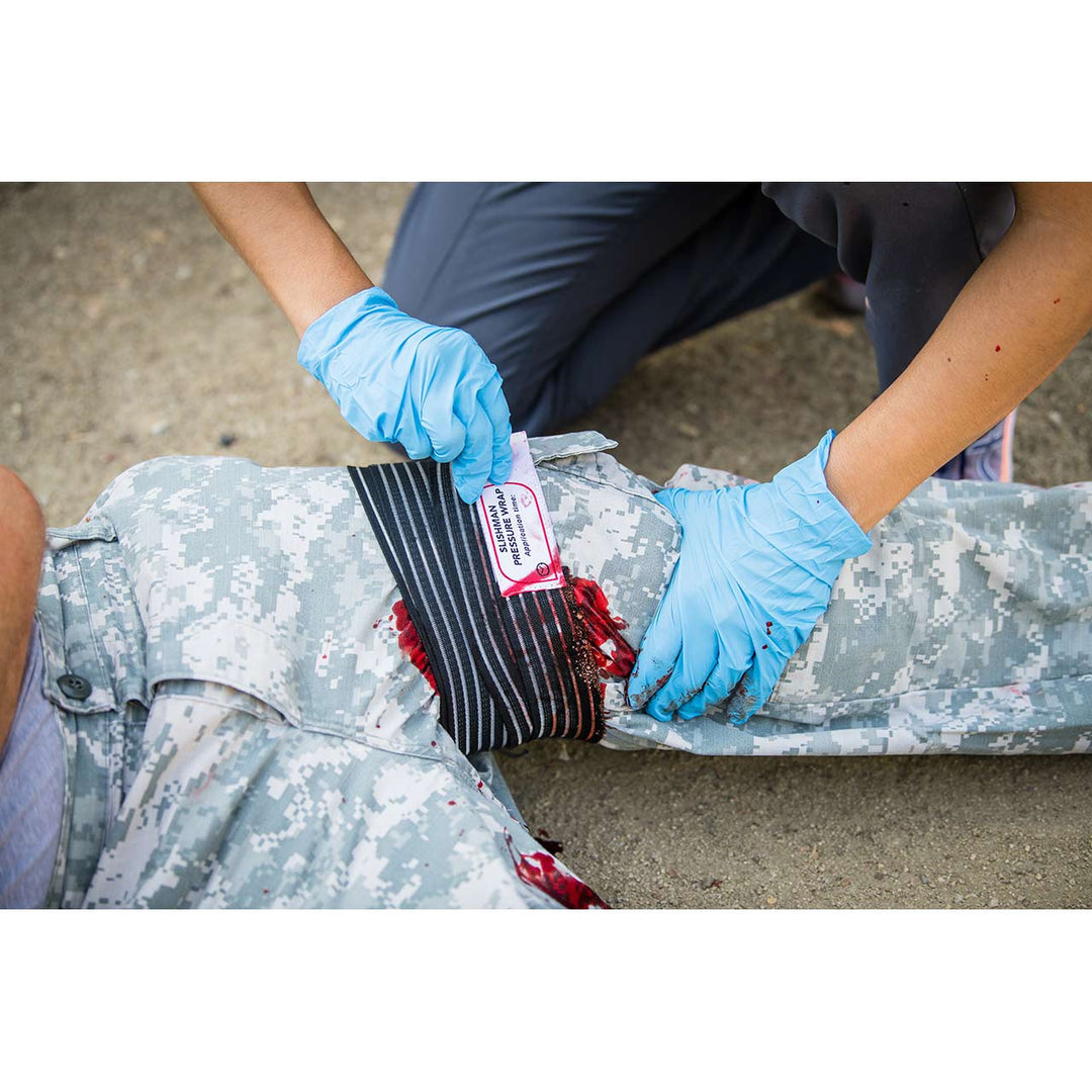 Field application of the wrap on an injured limb by a responder in a white shirt and gloves.