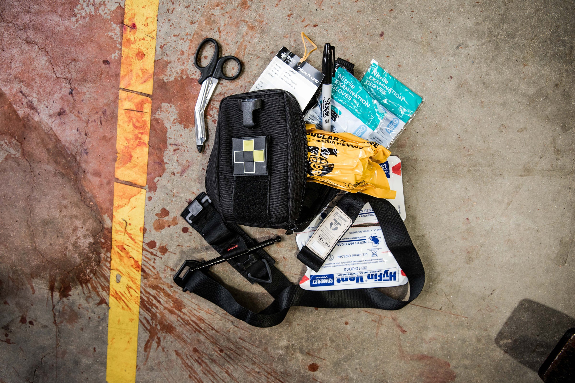 TacMed trauma pouch and medical supplies laid out on concrete including trauma shears, gloves, and casualty cards. Designed for fast access in field care. TacMed Australia – trusted for modular medical carry solutions.