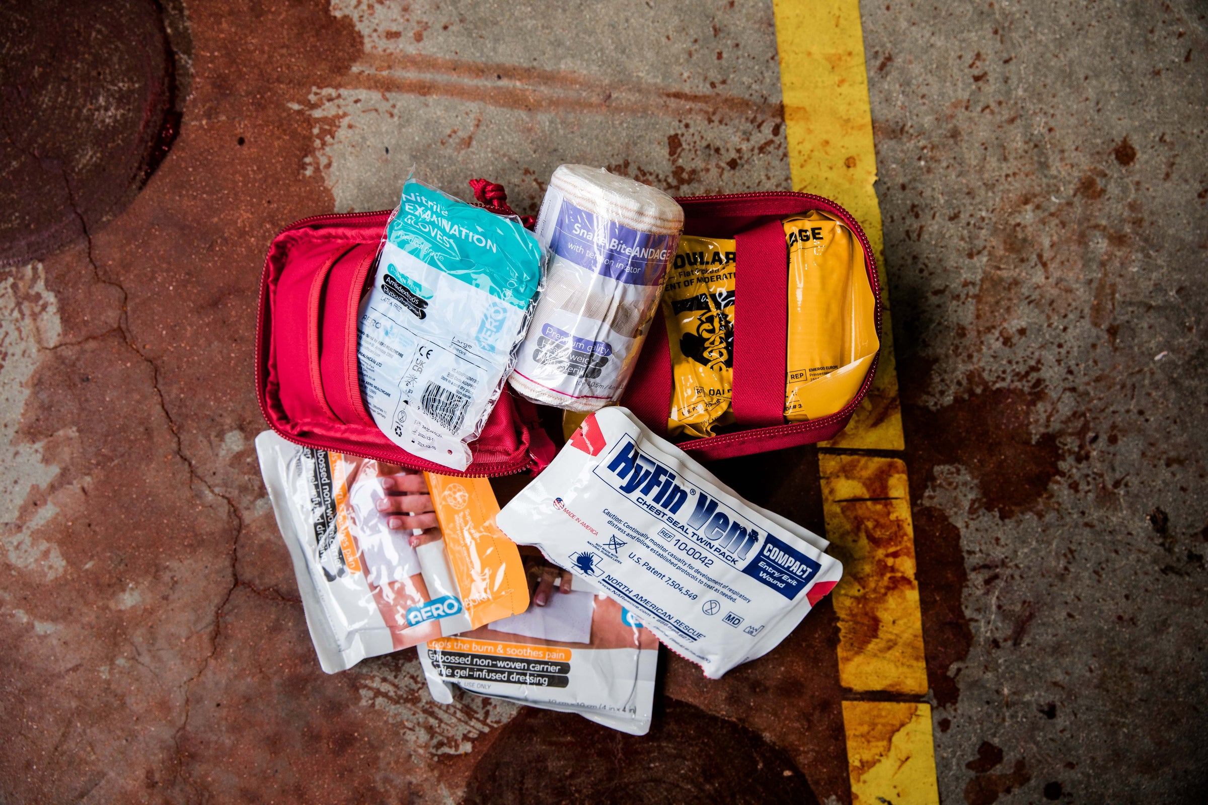 Red compact first aid kit opened on concrete, displaying gloves, bandages, and burn dressings. Designed for home, work, and remote emergencies. TacMed Australia – trusted for complete first aid kit solutions.
