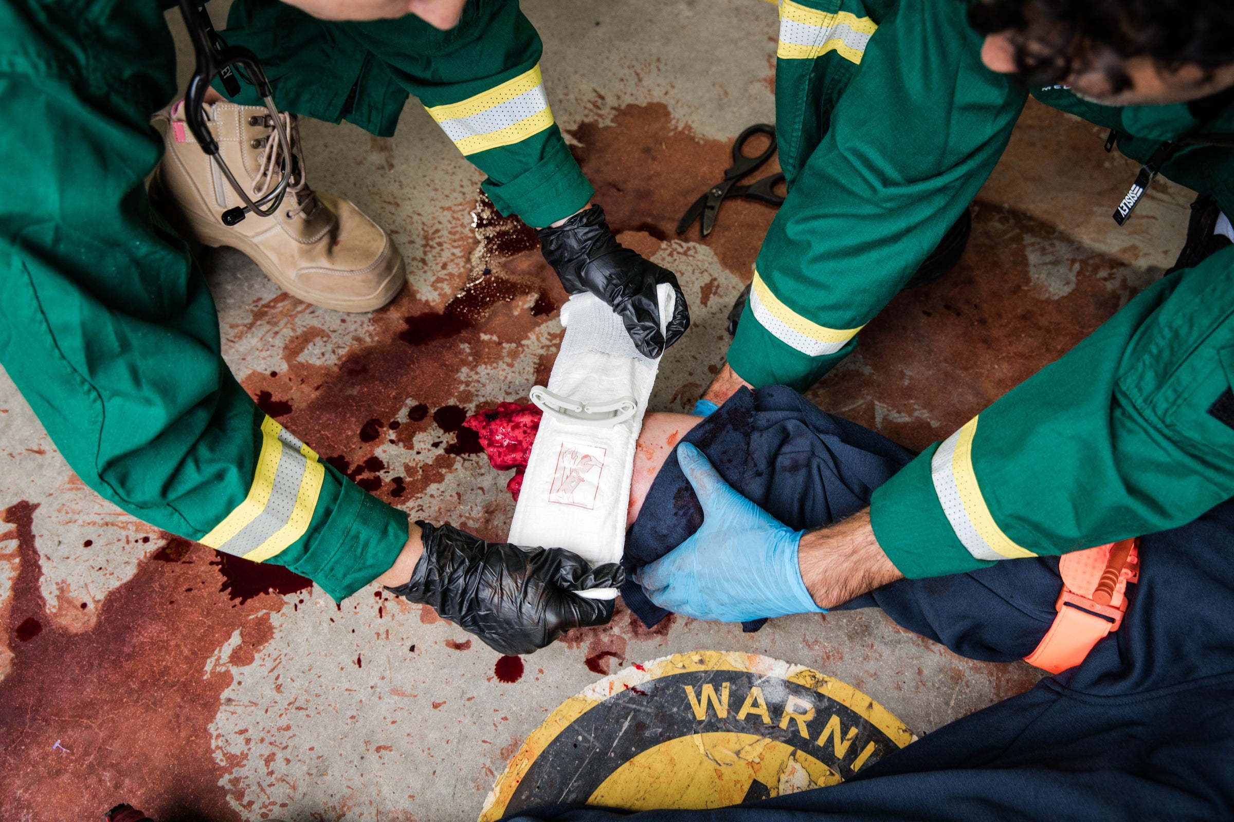 Paramedics applying tourniquet on simulated wound with visible blood and tactical boots. Designed for severe bleeding control in high-stress situations. TacMed Australia – trusted by tactical medics for hemorrhage management.