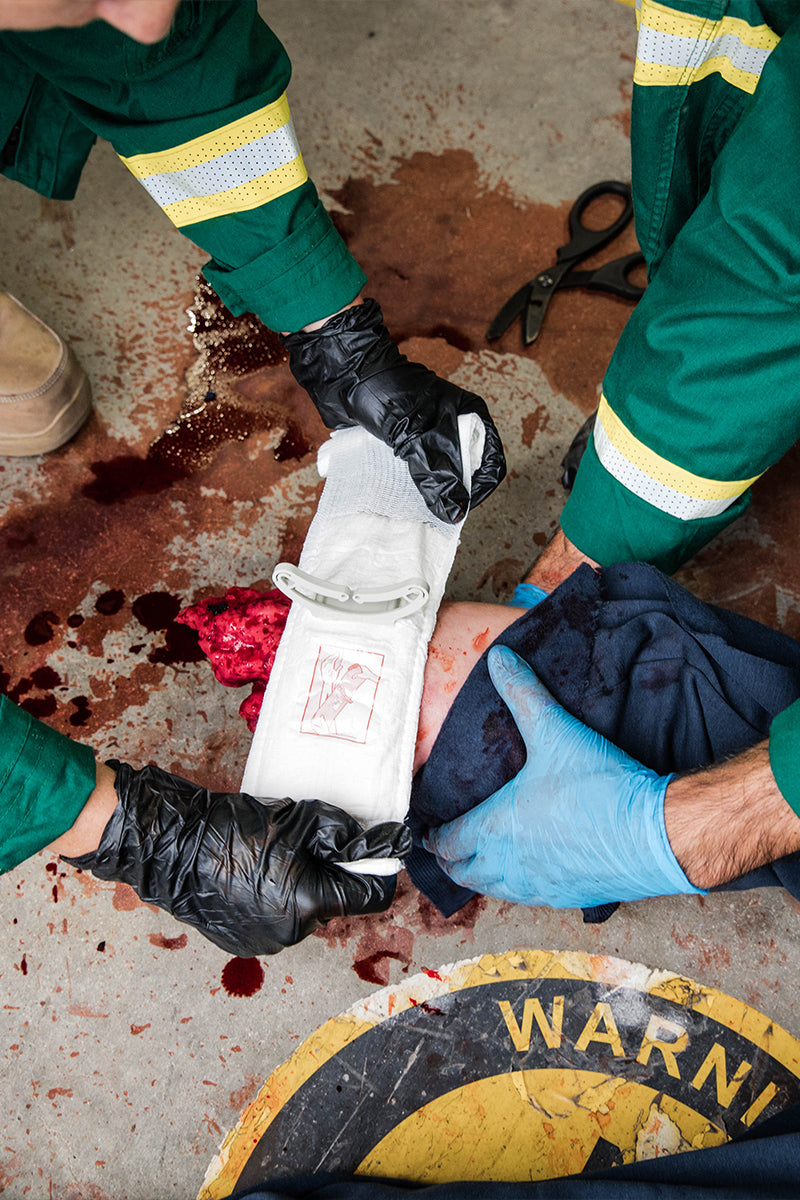 Paramedics applying tourniquet on simulated wound with visible blood and tactical boots. Designed for severe bleeding control in high-stress situations. TacMed Australia – trusted by tactical medics for hemorrhage management.