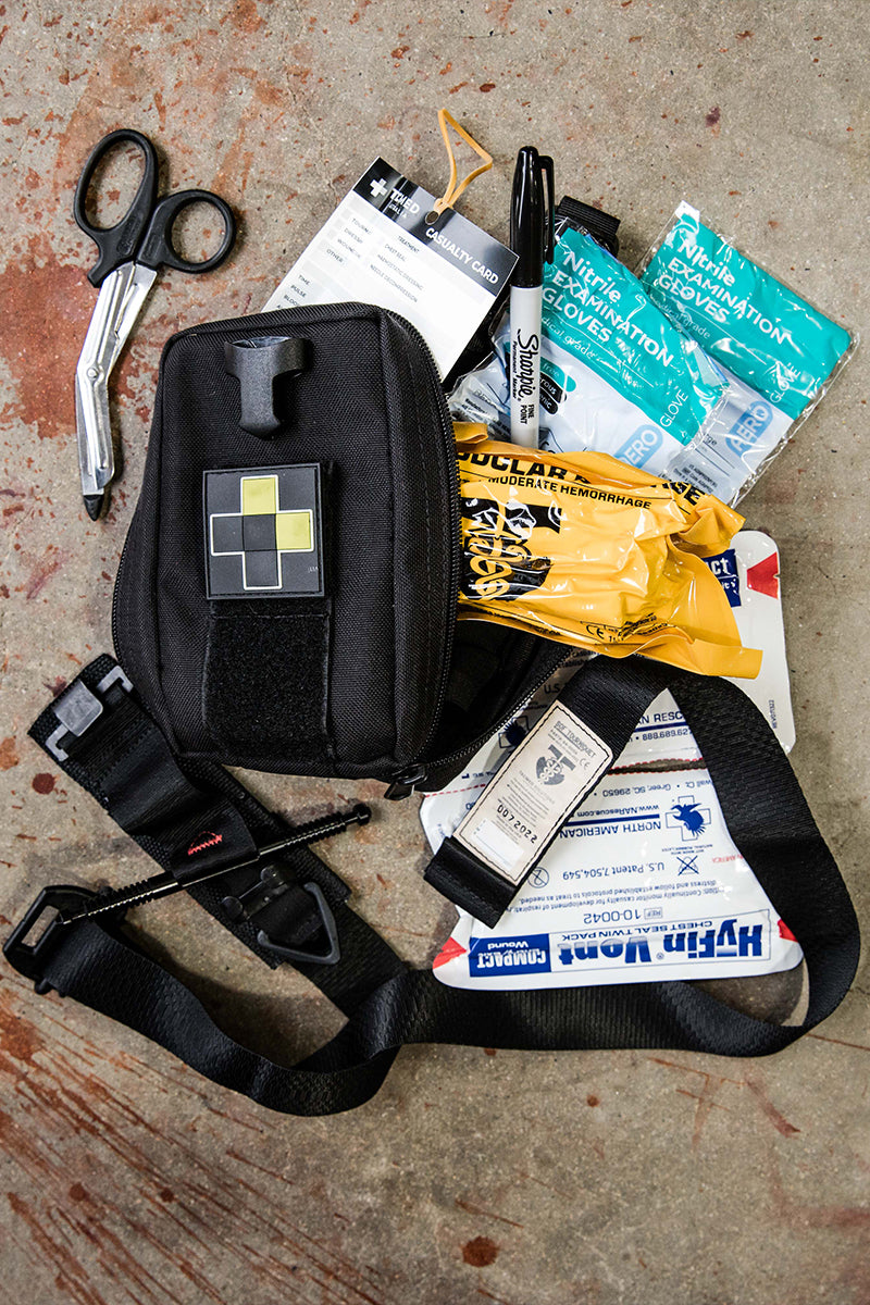 TacMed trauma pouch and medical supplies laid out on concrete including trauma shears, gloves, and casualty cards. Designed for fast access in field care. TacMed Australia – trusted for modular medical carry solutions.