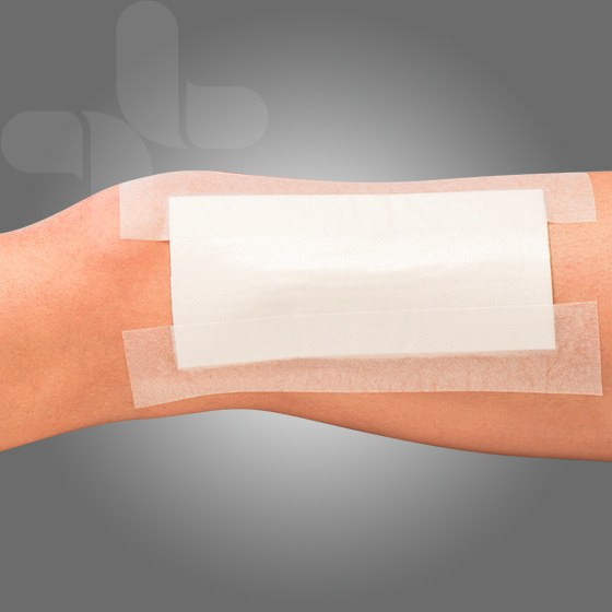 Close-up of white paper tape securing a medical dressing on a forearm.