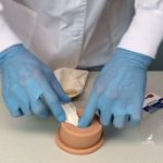 Instructor wearing blue gloves demonstrating wound packing on the TrueClot Basic Packing Trainer.