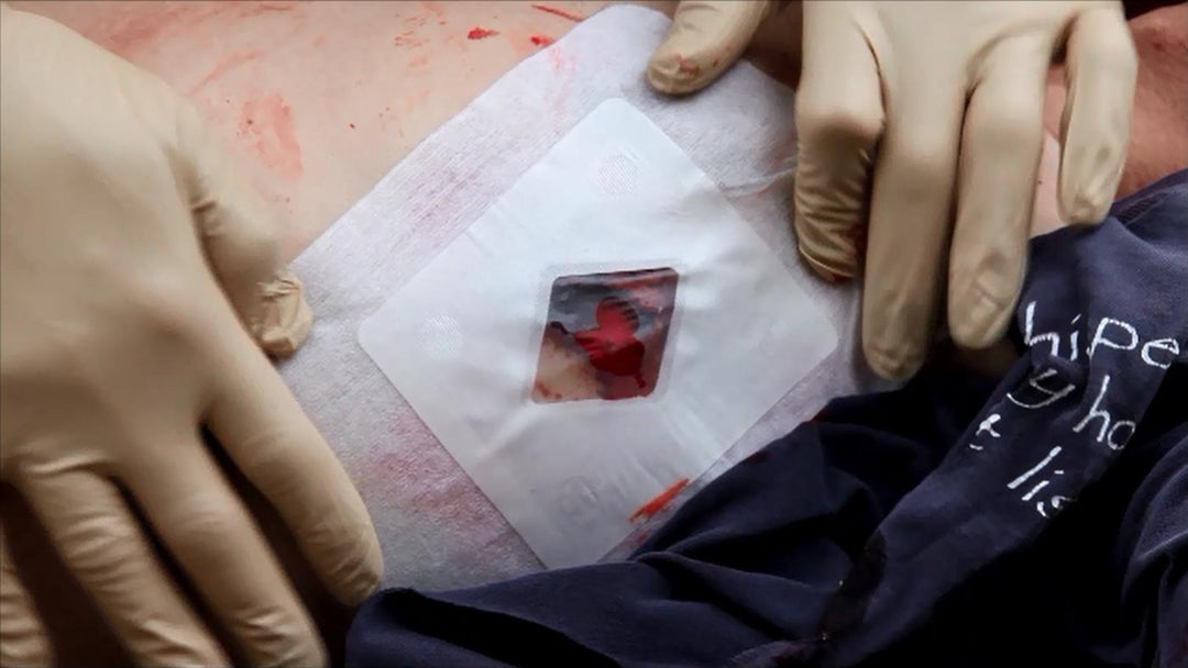 Gloved hands applying the Russell Chest Seal to a bleeding simulated chest wound during trauma care simulation.