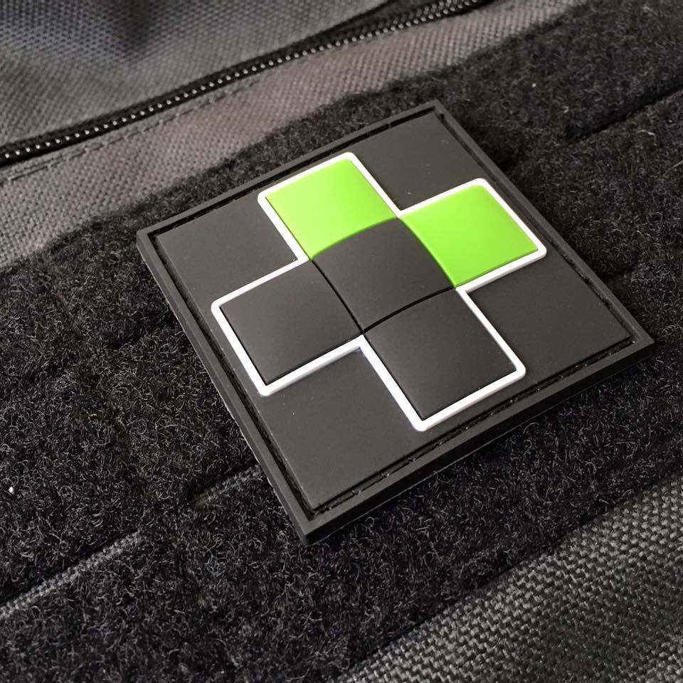 TacMed Patch featuring a black and green cross with white outline, securely attached to a tactical bag’s hook-and-loop panel. Designed for quick identification of medical kits and personnel.