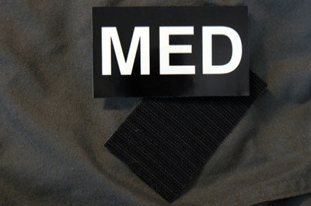 Glow-in-the-dark 'MED' patch attached to a black tactical uniform sleeve using Velcro backing.