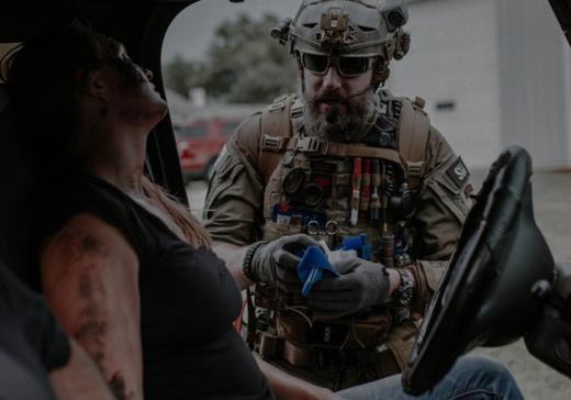 Tactical medical professional in full gear providing emergency medical care to a patient in a vehicle, featuring North American Rescue branding