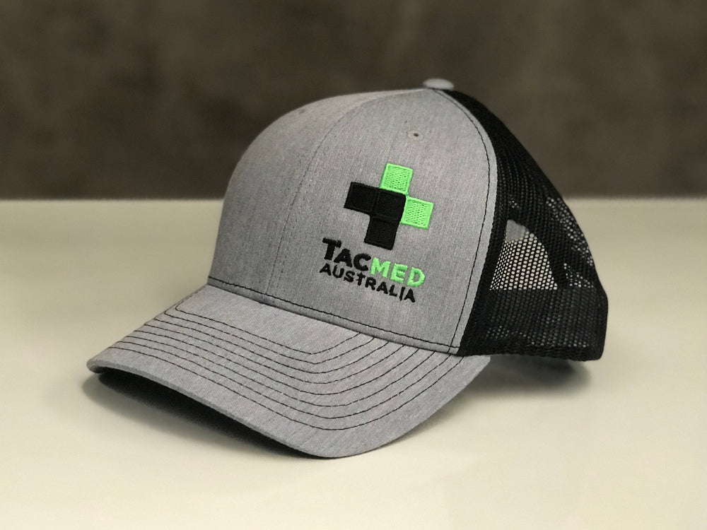 TacMed trucker cap displayed on a tabletop surface, showing front logo and mesh back design