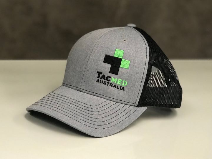 TacMed trucker cap displayed on a tabletop surface, showing front logo and mesh back design