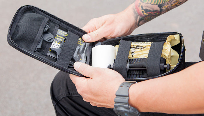 Person opening a black LAPD trauma kit pouch while seated, revealing packed medical supplies.