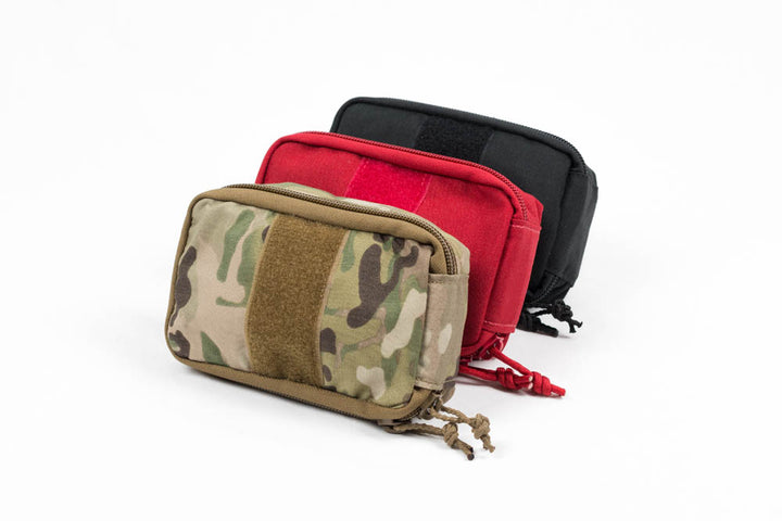 Three empty Operator IFAK pouches in camouflage, red, and black, arranged in a row on a white background.